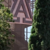 University A block logo in a metal frame with greenery around it. 