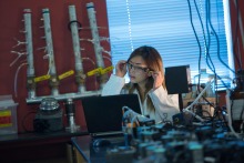 Image of a student in a lab wearing goggles and a white lab coat. 